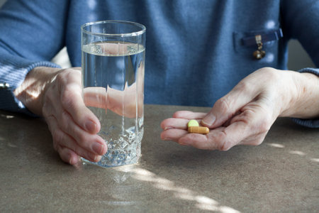 Closeup of elderly woman hand holding pills and glass of drinking water. Senior woman is going to take medicines for illnesses. Health problems in old age, taking certain medications. Medicineの写真素材