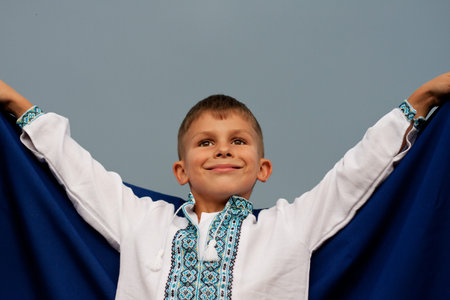 happy Ukrainian boy in embroidered shirt - vyshyvanka with blue-yellow flag of Ukraine, against sky....