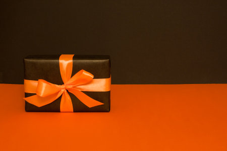 One rectangular gift box packed in black paper, decorated with an orange satin ribbon, on a black and orange backgroundの写真素材