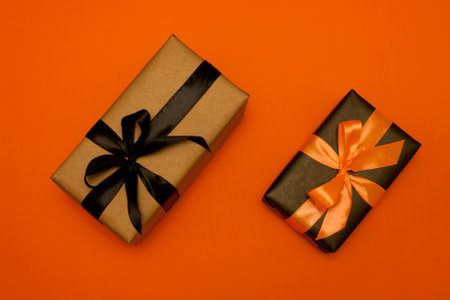 Two gift boxes of rectangular shape, wrapped in kraft paper and black paper, decorated with black and orange satin ribbon and bow, lie on orange background. Sale. Black Friday.の写真素材