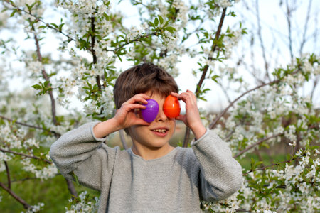 Happy easter. Cute funny preschooler boy with Easter eggs in garden, portrait against background of blooming tree. Laughing child during an Easter egg hunt. Holiday tradition. Spring, outdoorの写真素材