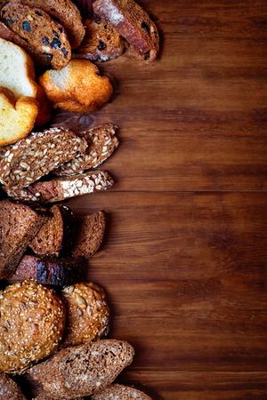 Assortment of baked bread on the background of a wooden table. seeds of wheat in a sieve and buckwheat seeds, spikelets of wheat and also oats and prunes. view from above. place for textの写真素材