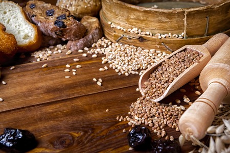 Assortment of baked bread on the background of a wooden table. seeds of wheat in a sieve and buckwheat seeds, spikelets of wheat and also oats and prunes. view from above. place for textの写真素材