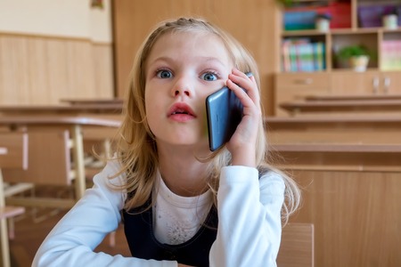 A first grade student at school speaks by phone. emotions of schoolgirlsの写真素材