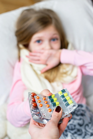 A sick little girl takes medication and eats fruit.の写真素材