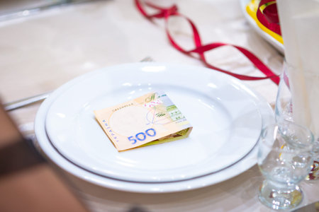 A folded banknote rests on a white plate, surrounded by elegant table settings and festive decor.