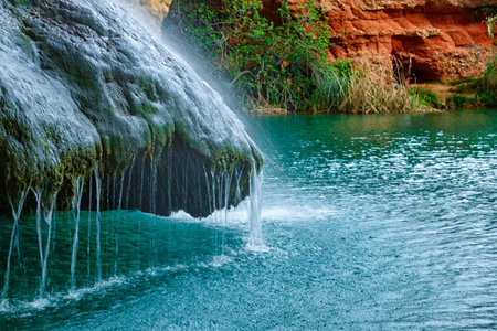 Refreshing Waterfall Cascading Into a Serene Turquoise Pool Surrounded by Greenery at Sunsetの写真素材