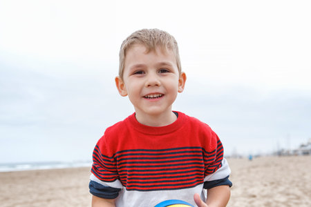 Young Boy Playing With a Colorful Beach Ball on a Sandy Shoreline During a Cloudy Afternoonの写真素材