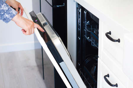 female hand is switching on off a modern built-in dishwasherの写真素材