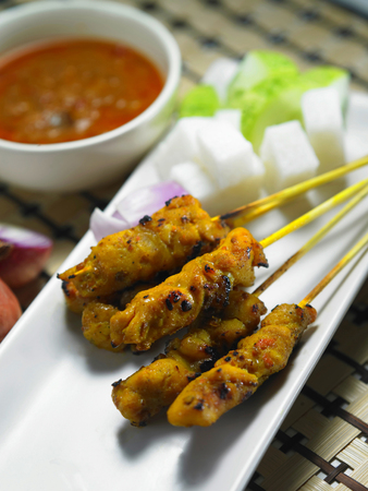 Malaysia food- six sticks of satay, ketupat cubes and cut cucumbers on a plate with a bowl of curry by the sideの写真素材