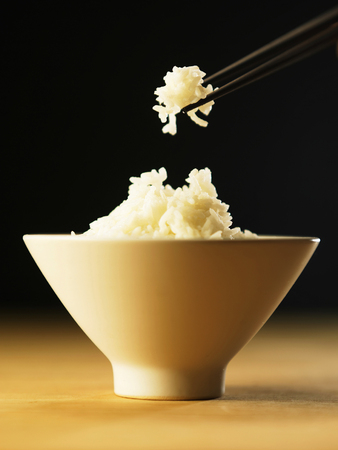 bowl of white rice with a pair of chopsticks taking some of the riceの写真素材