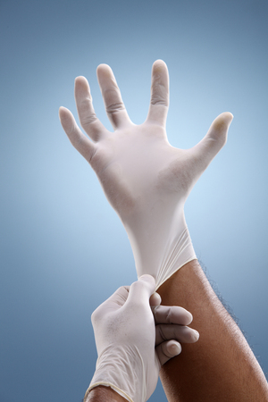 Hands putting on surgical gloves over a creative blue background.の写真素材