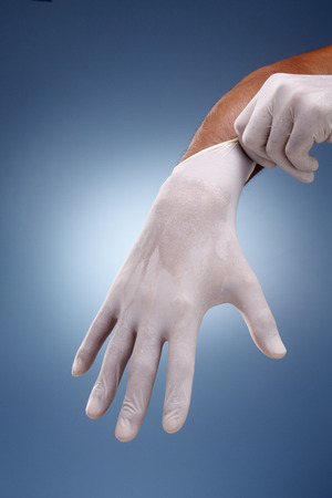 Hands putting on surgical gloves over a creative blue background.の写真素材