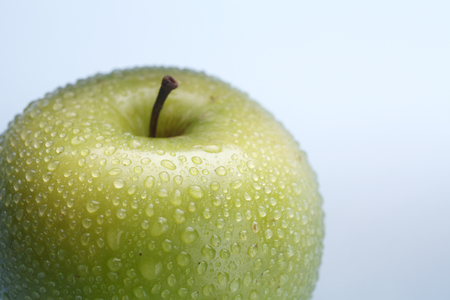Wet green apple covered by water drops on coloured background. Isolation.の写真素材