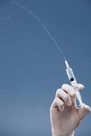 Hand holding syringe isolated on coloured background.の写真素材
