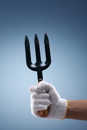 Hand holding garden pitchfork on coloured background.の写真素材