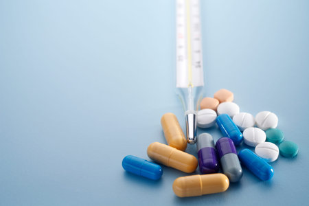 Mecury thermometer with pills isolated on blue background.