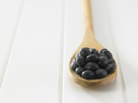 Black beans with wooden spoon on white tableの写真素材