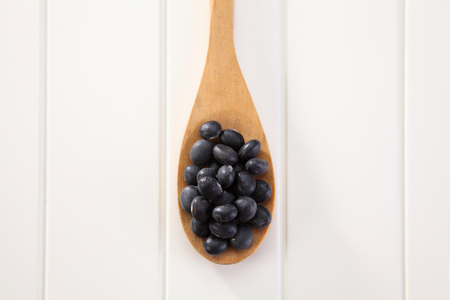 Black beans with wooden spoon on white tableの写真素材