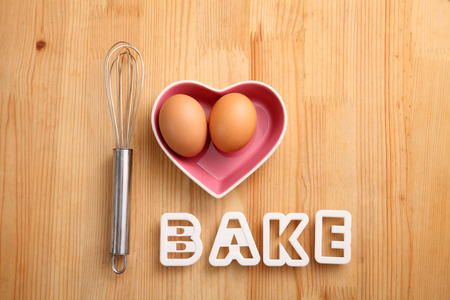 baking concept hand whisk next to eggs in a heart shape containerの写真素材