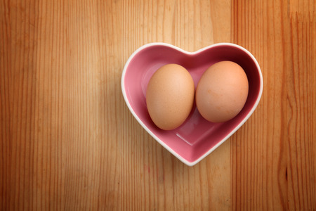Heart-shaped pottery and eggs on wooden backgroundの写真素材