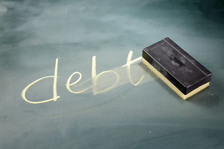 word DEBT written in chalk on a blackboard being rubbed out by an eraserの写真素材