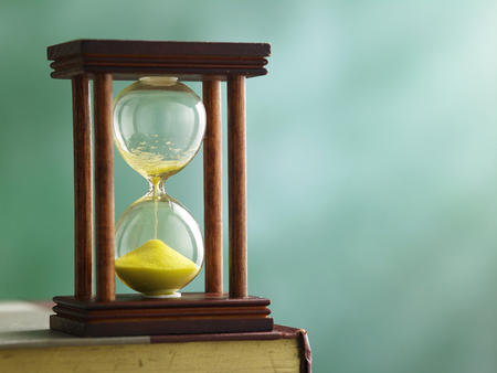 hourglass on top of book in front of black boardの写真素材