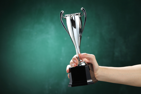 hand holding up a silver trophy cup as a winner in a competitionの写真素材