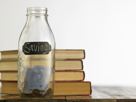 saving jar with stack of books on the wooden tableの写真素材