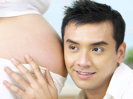 close up of man put his ear to wife tummy