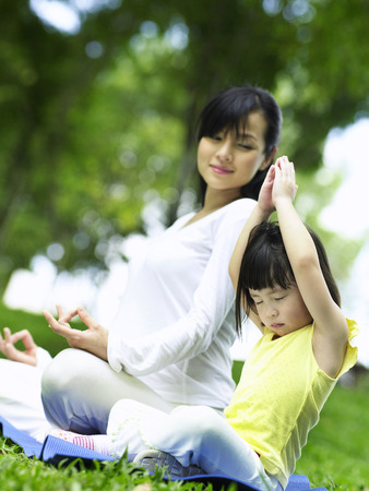 mother looking at daughter practising yogaの写真素材
