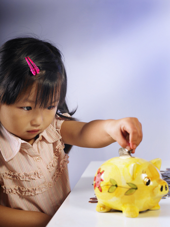 girl putting money into piggy bankの写真素材