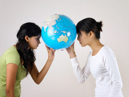 two young woman face to face using forehead holding a globe together