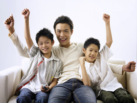 father and two sons raising arms at living hall while watching tvの写真素材