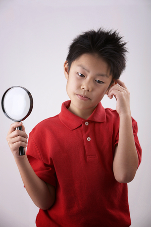 boy holdiing a magnifier on the plain backgroundの写真素材