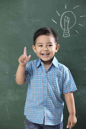 malay boy standing in front of the blackboard with light bulb drawingの写真素材