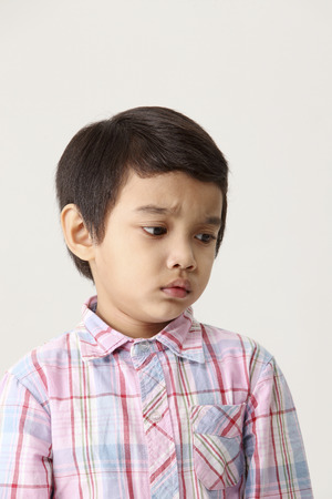 Portrait of young boy in checkered shirt on white backdrop,sadの写真素材