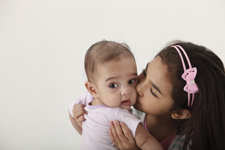 young girl holding her baby sister closelyの写真素材