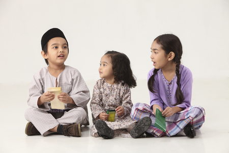 sisters and brother sitting in a row holding a green packetの写真素材
