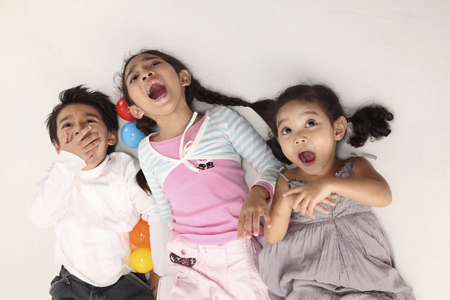 Three children lying on backs on ground shoutingの写真素材