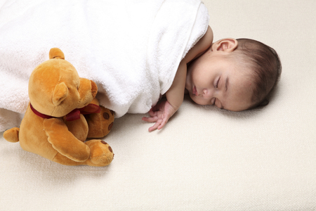 close up of Newborn laying in white blanket with teddy bearの写真素材
