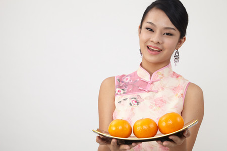 Smiling Chinese woman dress traditional cheongsam holding plate of mandarin orangesの写真素材