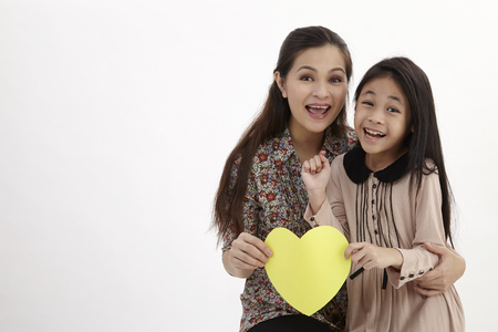 mother and daughter holding a yellow blank heart shape card boardの写真素材