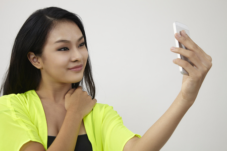 Pretty girl take a self portrait with her smart phone. Asian girl selfie, isolated on white background.の写真素材