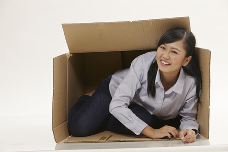 asian woman try to fit gerself to a small boxの写真素材