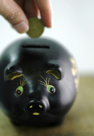 Inserting coin into a piggy bankの写真素材