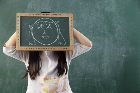 girl holding black board with funny face drawingの写真素材