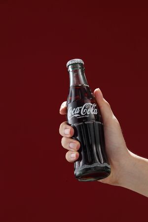 Kuala Lumpur,Malaysia 11th July 2016, Hand hold a bottle Coca-Cola on red background. Coca Cola drinks are produced and manufactured by The Coca-Cola Company.のeditorial素材