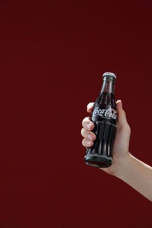 Kuala Lumpur,Malaysia 11th July 2016, Hand hold a bottle Coca-Cola on red background. Coca Cola drinks are produced and manufactured by The Coca-Cola Company.のeditorial素材