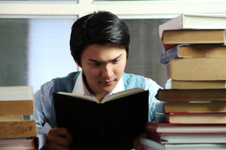 Young man reading by piled books,